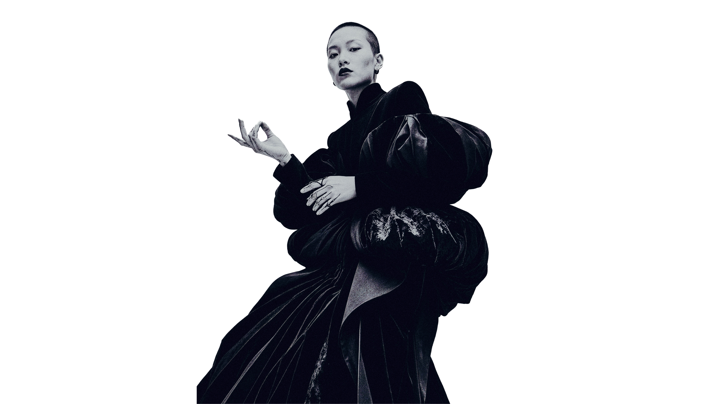 Low-angle high-fashion editorial portrait of an Asian model with a buzzed cut and dark makeup, wearing a voluminous black velvet avant-garde gown and holding a sculptural metal hand piece against a white studio background realized Alessandro Valori Sbranzo Studio Vago