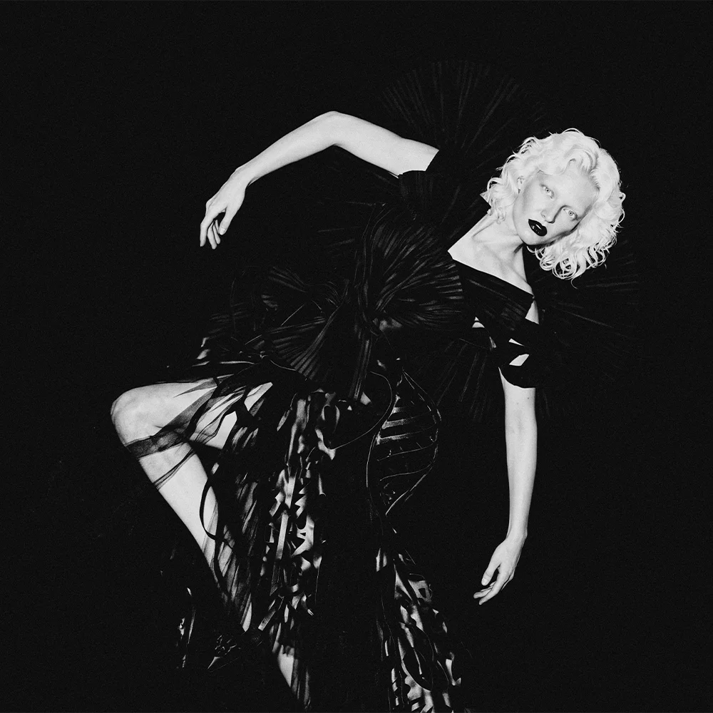 Black and white editorial of Elena arched in a radial pleated black gown with raised arm against a black background – Sbranzo Alessandro Valori Studio Vago Elena