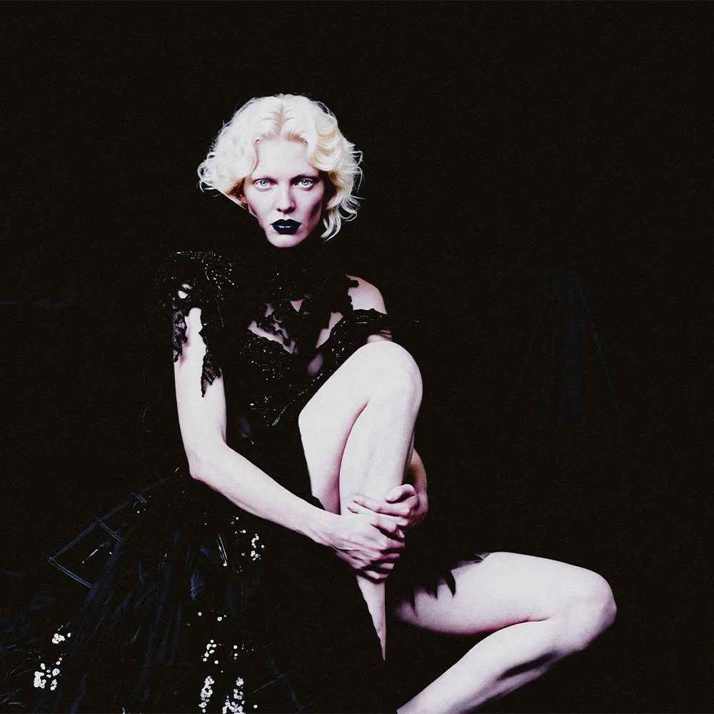 Editorial portrait of Elena seated with raised knee wearing a black sequined lace gown with blue lips – Sbranzo Alessandro Valori Studio Vago Elena