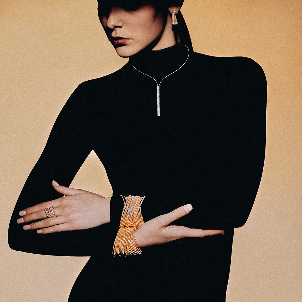 Fashion jewelry editorial 999 – model wearing a Y-necklace, tassel earrings, wide fringe bracelet and ring against a camel background – Sbranzo Alessandro Valori Studio Vago Viola Sgriscia