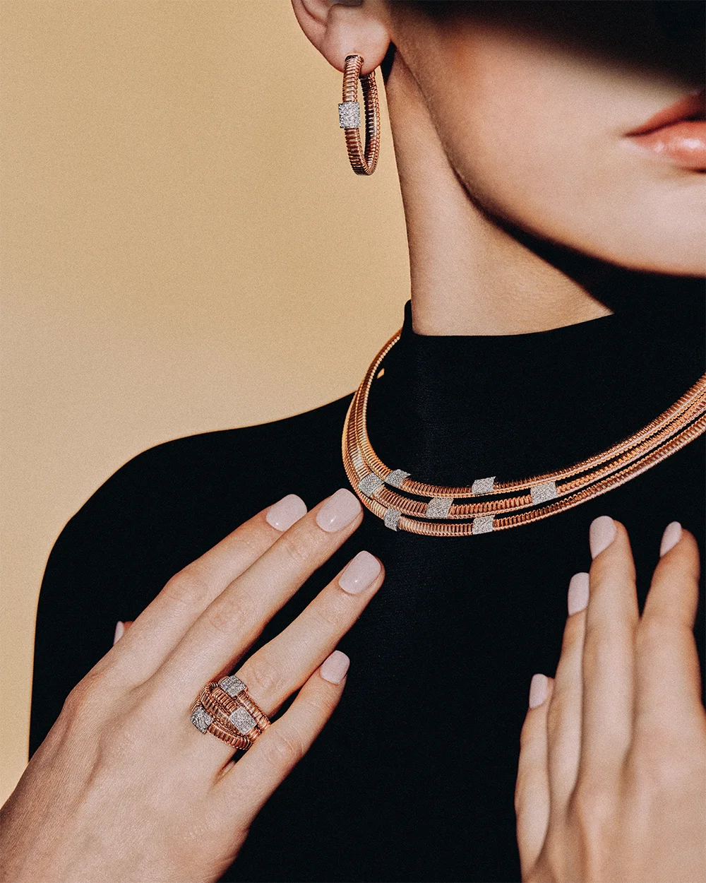 Fashion jewelry editorial 999 – model wearing gold hoop earrings, a wide woven gold bracelet and ring against a camel background – Sbranzo Alessandro Valori Studio Vago Viola Sgriscia