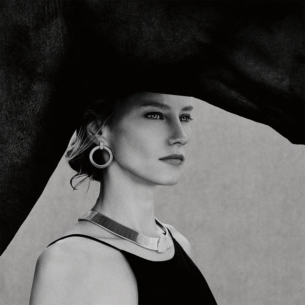 Black and white fashion jewelry editorial 999 – close-up portrait of a model wearing a hoop earring and rigid necklace against a horse backdrop – Sbranzo Alessandro Valori Studio Vago Valeria Miro
