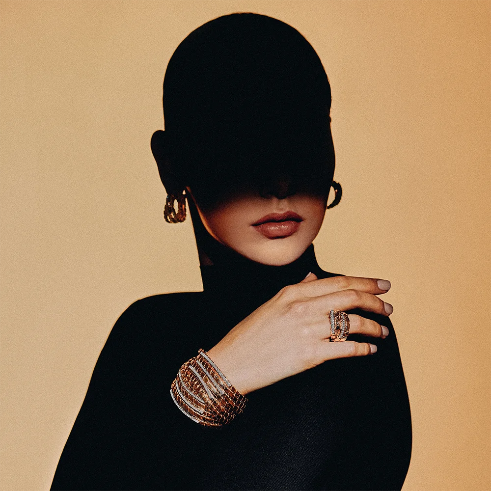 Fashion jewelry editorial 999– semi-silhouette of a model wearing hoop earrings, a wide woven bracelet and ring against a camel background – Sbranzo Alessandro Valori Studio Vago Viola Sgriscia
