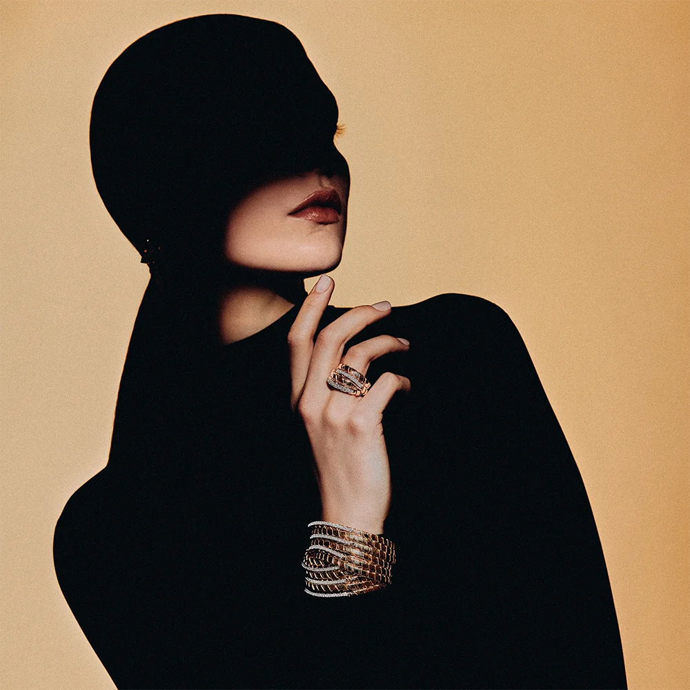 Fashion jewelry editorial 999 – semi-silhouette of a model wearing a wide multi-strand bracelet and diamond ring against a camel background – Sbranzo Alessandro Valori Studio Vago Viola Sgriscia