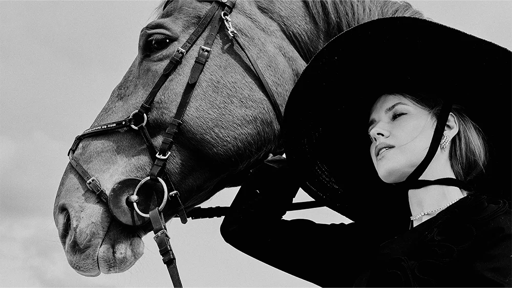 Fashion jewelry advertising Fabiani – black and white portrait of a blonde model in a wide-brim hat resting against a horse, wearing a diamond earring and necklace – Sbranzo Alessandro Valori Studio Vago