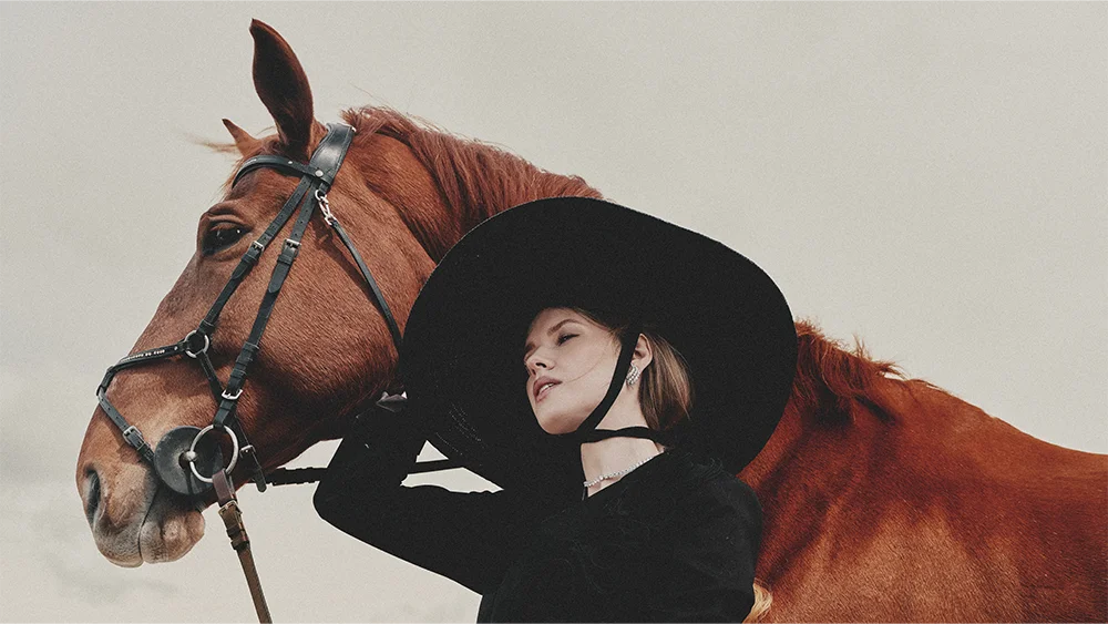 Fashion jewelry advertising Fabiani – blonde model in a wide-brim hat resting against a chestnut horse, wearing a diamond earring and necklace – Sbranzo Alessandro Valori Studio Vago