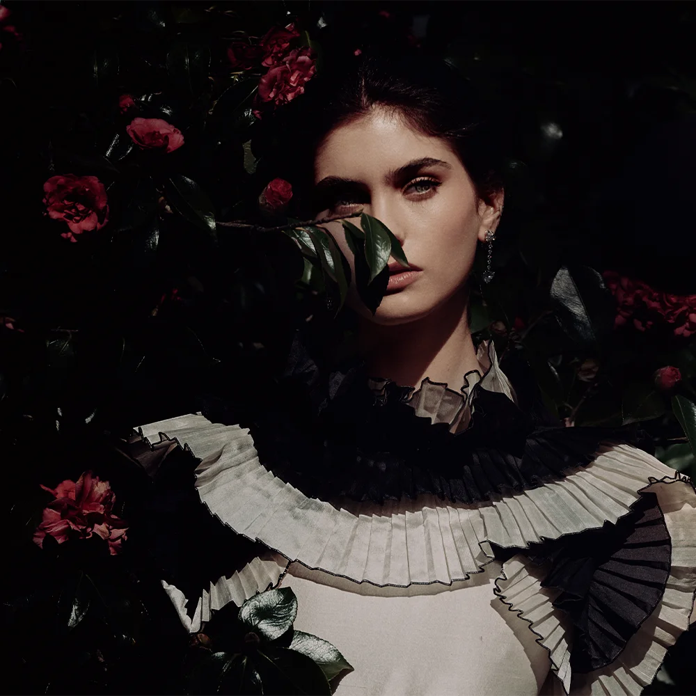 Editorial fashion jewelry portrait of a model among red camellias wearing a pleated ruffle collar and a drop earring – Fabiani Gioiellerie – Sbranzo Alessandro Valori Studio Vago Gaia Schiralli
