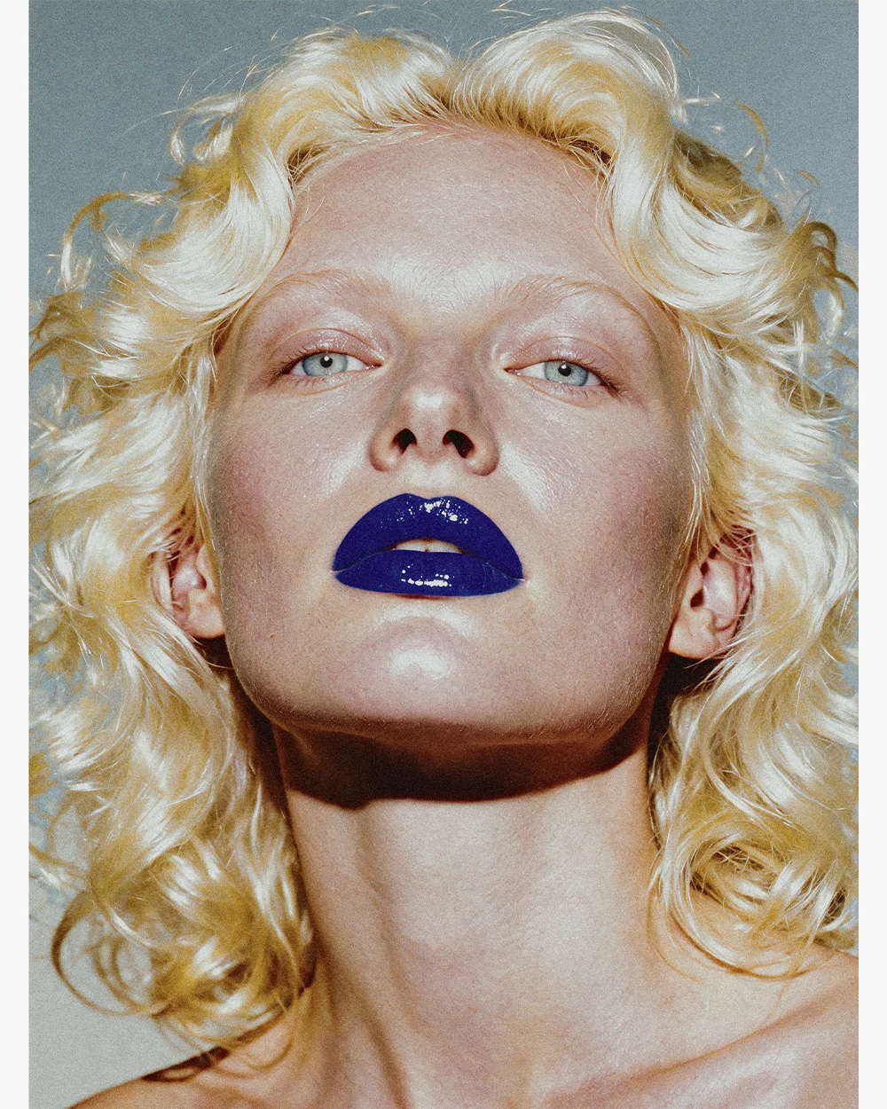 Editorial beauty close-up of Elena with glossy blue lips looking upward against a cold grey-blue background – Sbranzo Alessandro Valori Studio Vago Elena
