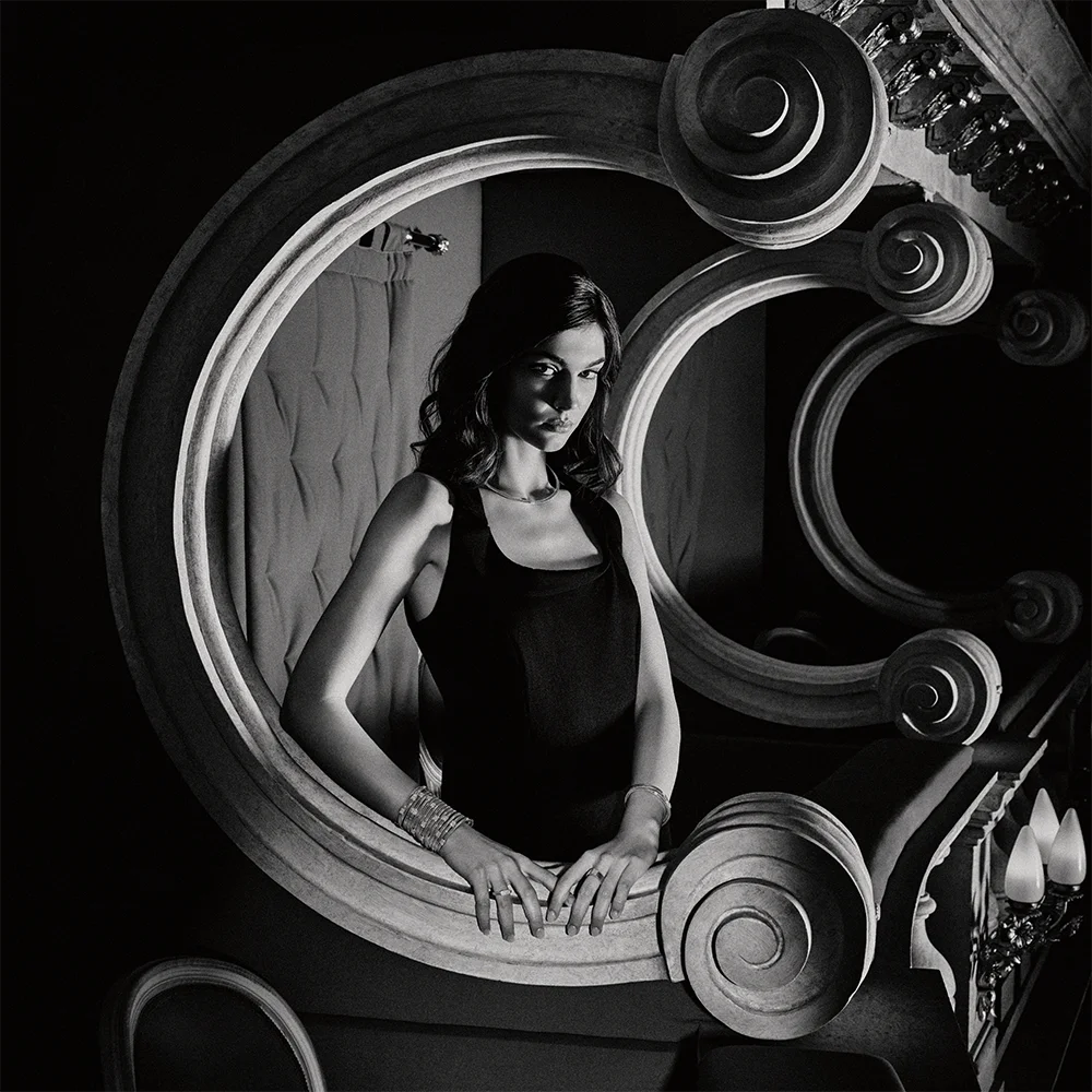 Black and white fashion jewelry editorial 999 – model in a black dress wearing bracelets and a ring framed by an ornamental C-shaped arch – Sbranzo Alessandro Valori Studio Vago Tati Janusheva