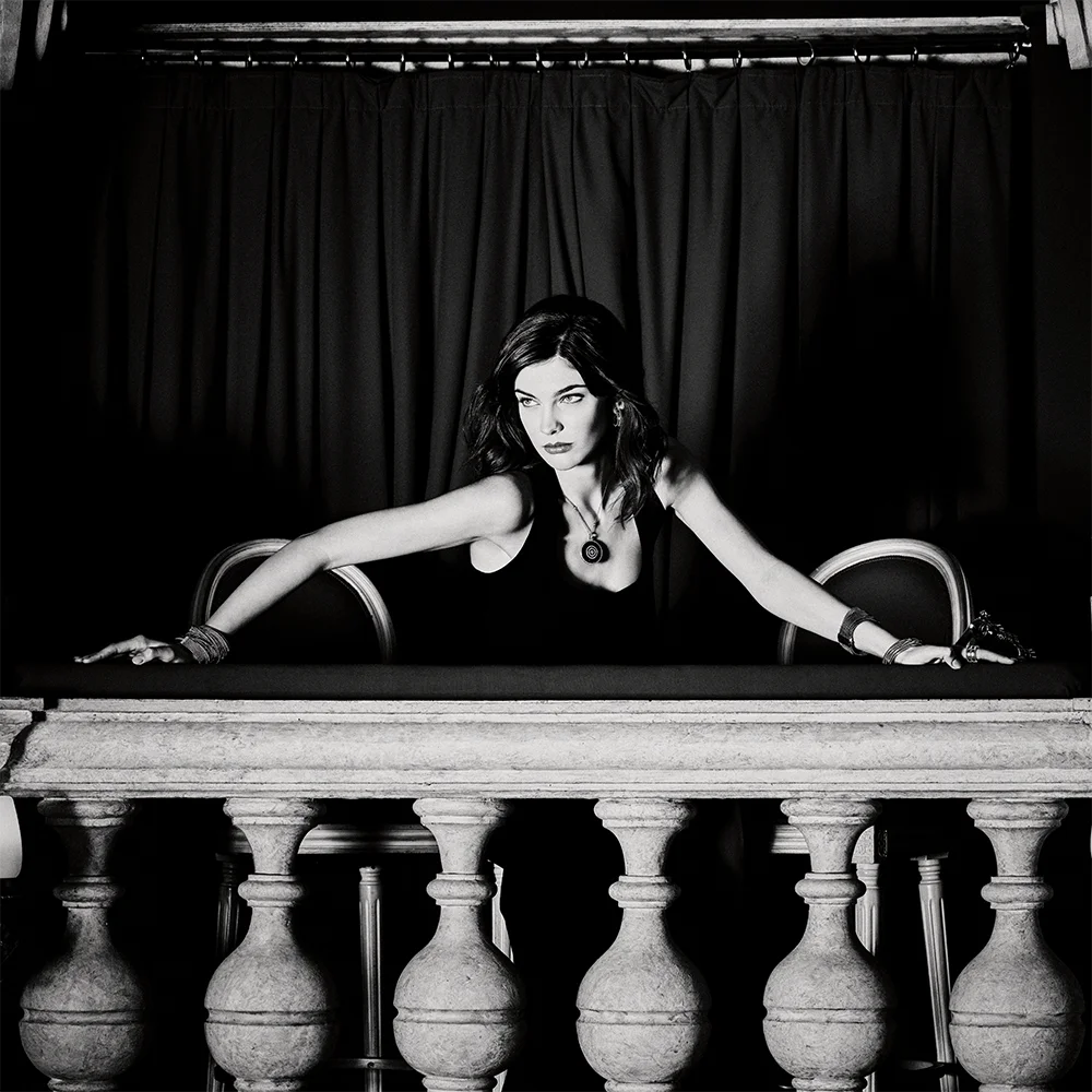 Black and white fashion jewelry editorial 999 – model in a black dress wearing a circular pendant necklace and bracelets leaning over a theatre balustrade – Sbranzo Alessandro Valori Studio Vago Tati Janusheva
