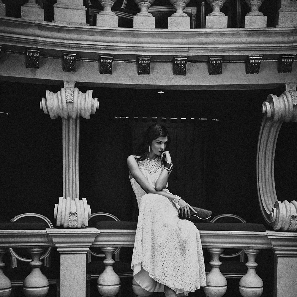 Black and white fashion jewelry editorial 999 – full-length model in a white lace dress wearing a necklace, bracelet and earring in a theatre interior – Sbranzo Alessandro Valori Studio Vago Tati Janusheva