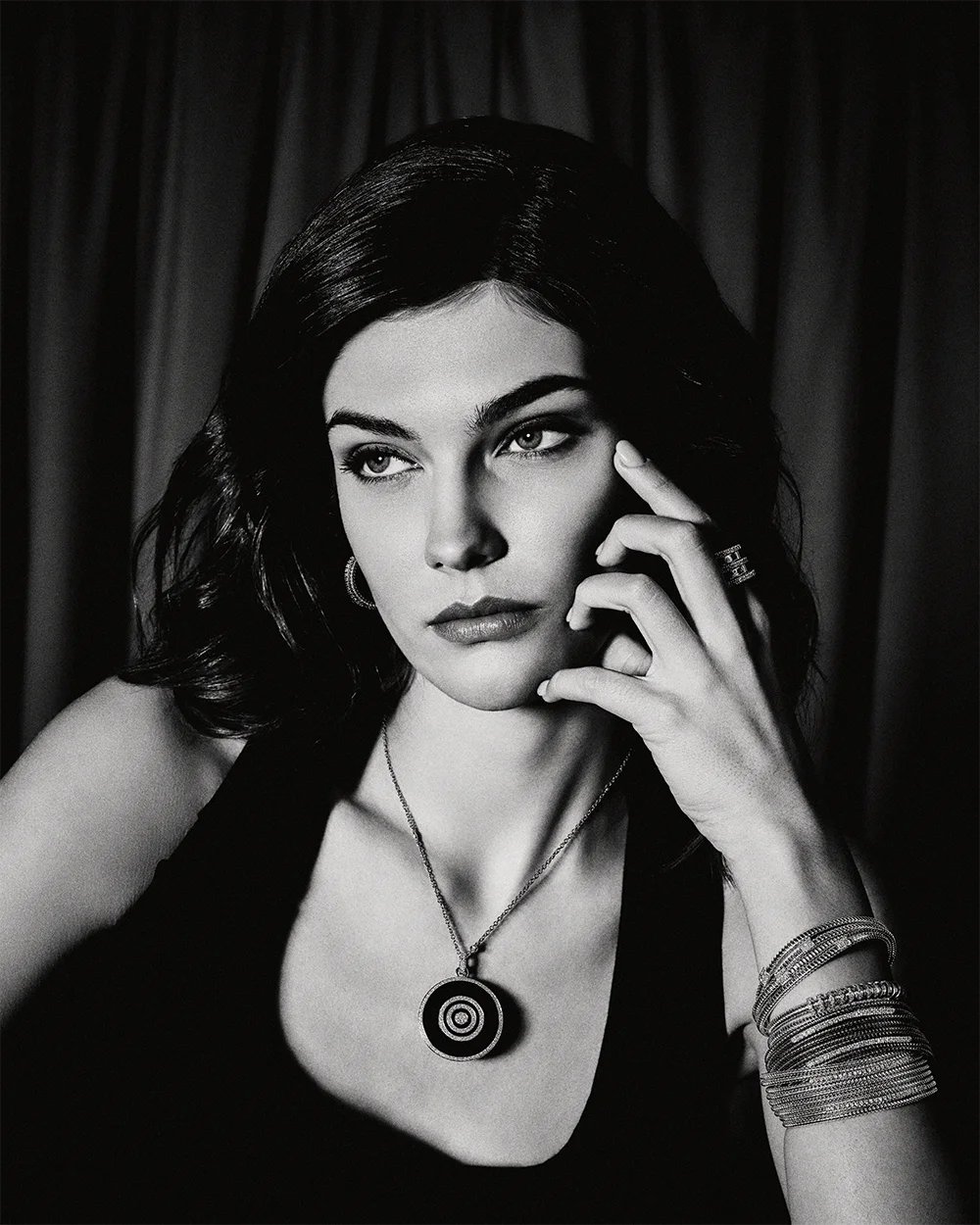 Black and white fashion jewelry editorial 999 – dramatic portrait of a model wearing a circular pendant necklace, stacked bracelets and ring against dark curtains – Sbranzo Alessandro Valori Studio Vago Tati Janusheva