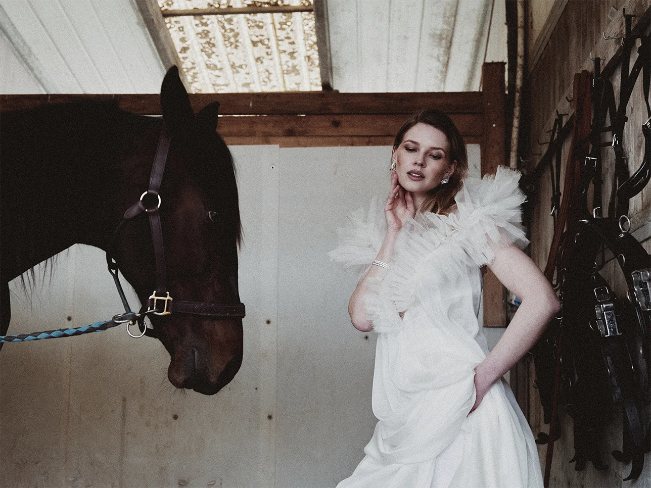 Fashion jewelry editorial Fabiani Gioiellerie – model in profile resting her hand on a horse's muzzle wearing a pear-cut diamond ring and diamond tennis bracelet in a brown leather coat – Sbranzo Alessandro Valori Studio Vago