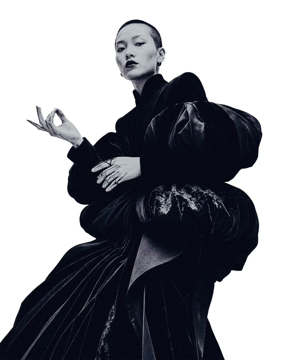Editorial portrait of a shaved-head model in a sculptural black velvet gown making a hand gesture against a white background – Sbranzo Alessandro Valori Studio Vago Yumi