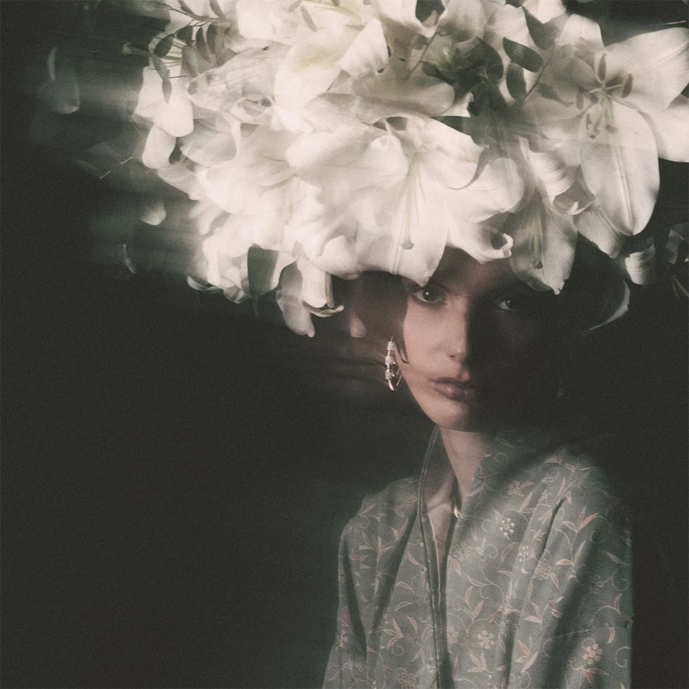 Editorial 999 – double-exposure portrait of a model with a white lily headpiece and hoop earring, floral patterned kimono, dark chiaroscuro background – Sbranzo Alessandro Valori Studio Vago